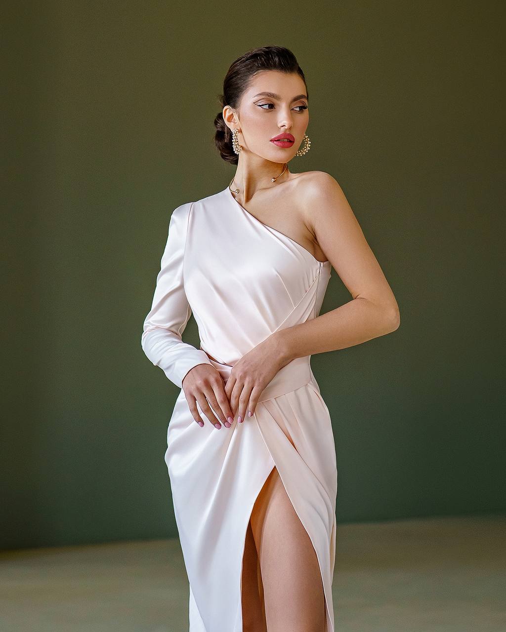 Woman wearing a white one-shoulder dress with a slit on a plain background