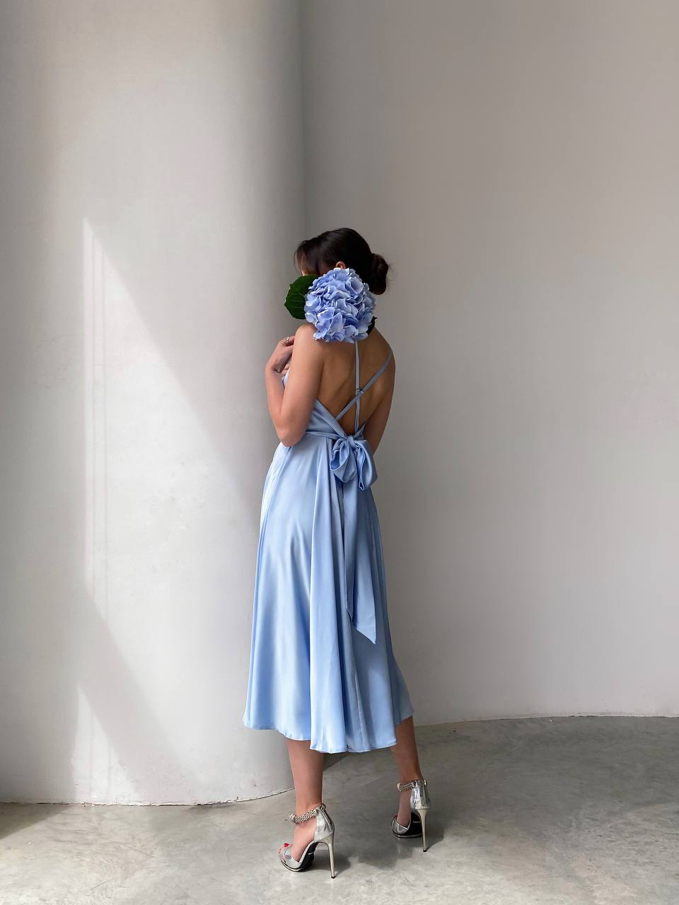 Woman in a light blue dress holding flowers against a plain wall