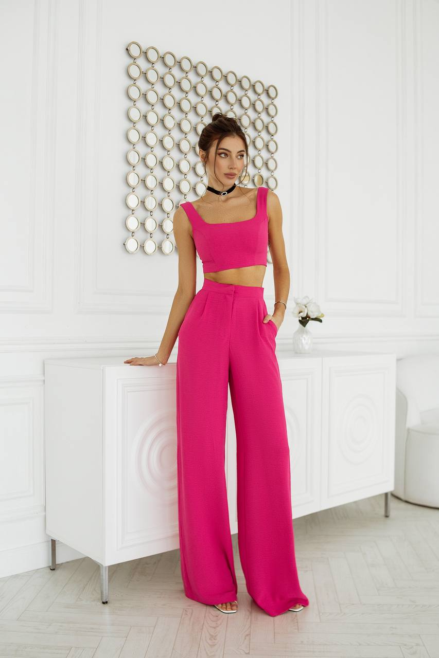 Woman in a bright pink outfit standing against a white wall with decorative elements.