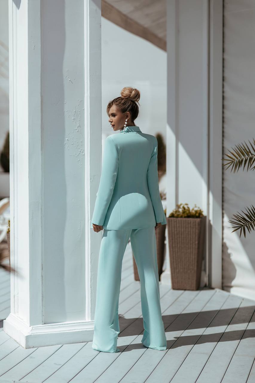 Woman in a light blue suit standing on a wooden deck with white columns.