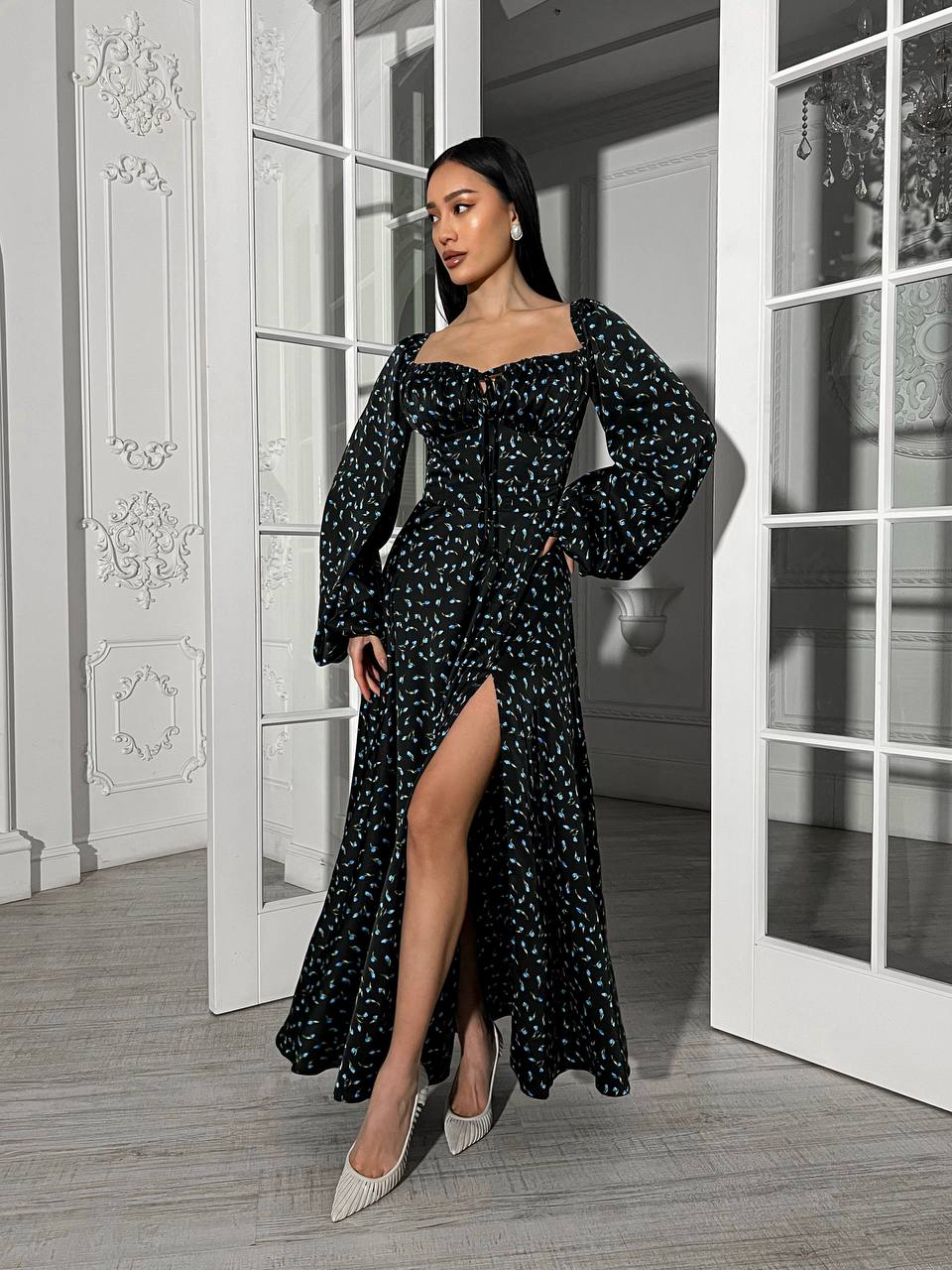 Woman in a black floral dress standing in a room with white walls and large windows.