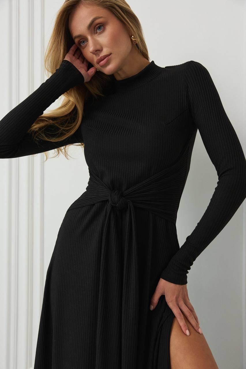 Woman wearing a black long-sleeve dress with a knot detail against a white background
