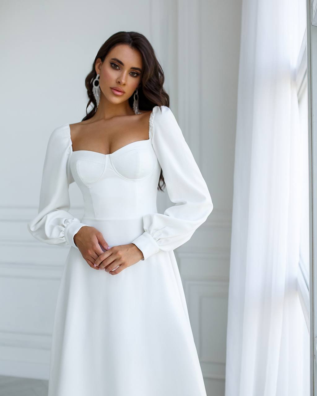 Woman wearing a white dress with long sleeves in a minimalistic setting