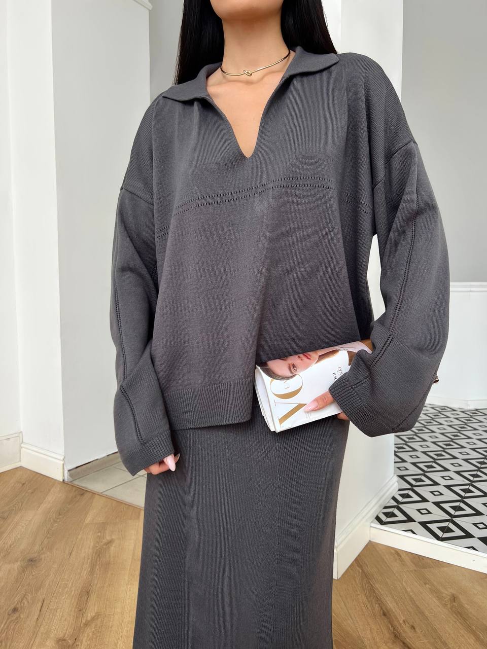 Person wearing a gray sweater and skirt holding a white clutch.