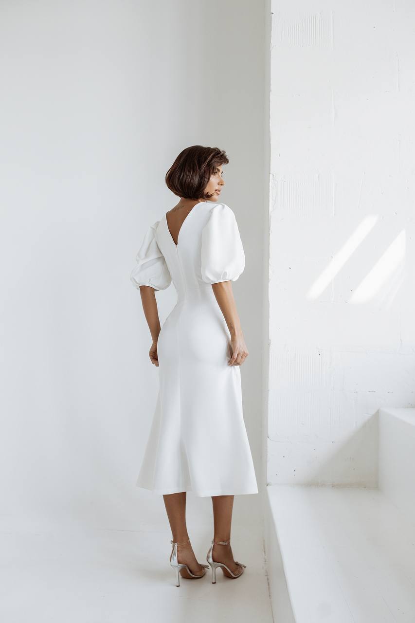 Woman wearing a white dress standing against a white wall.