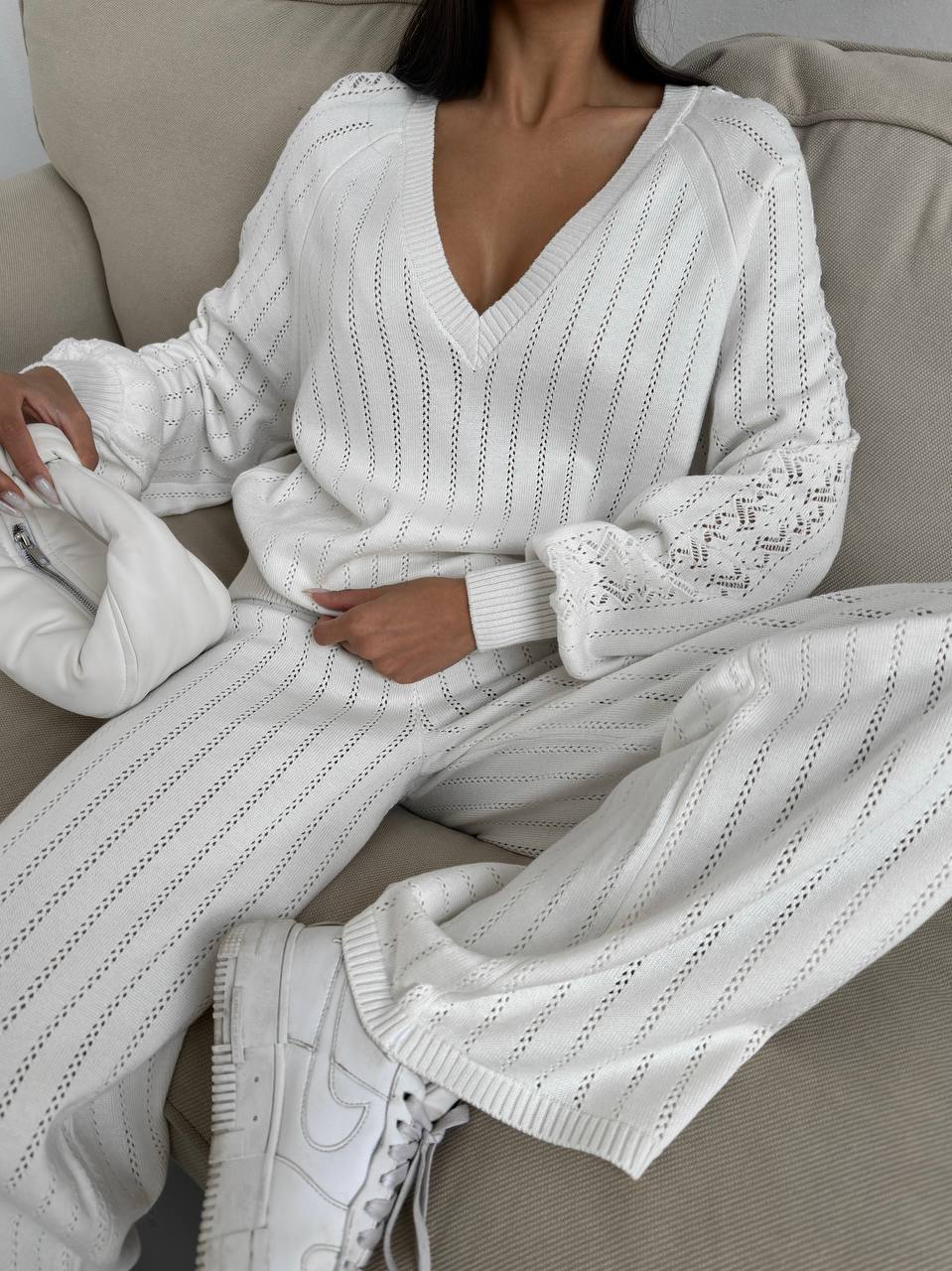 Person wearing a white knit outfit sitting on a couch.