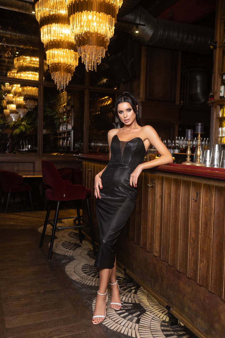 Woman in a black dress standing in a bar with chandeliers and wooden decor.