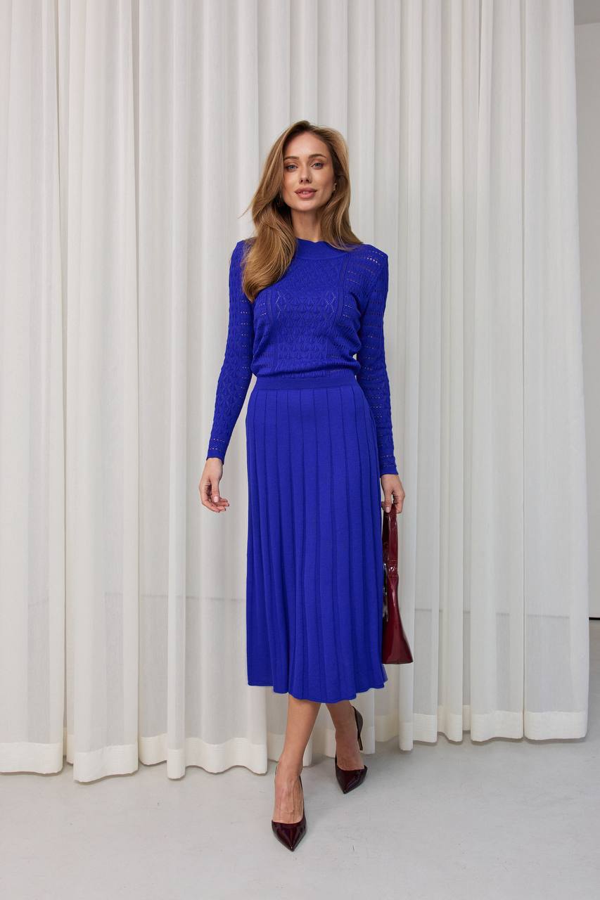 Woman wearing a blue outfit standing in front of white curtains