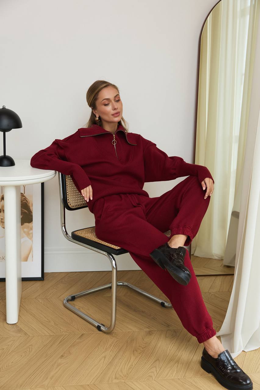 Woman in a red outfit sitting on a chair in a room with a mirror and lamp.