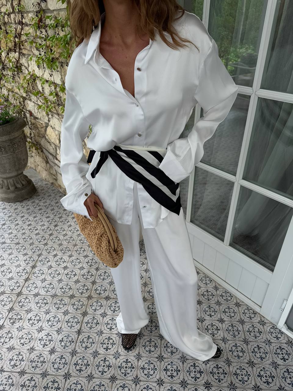 Woman wearing a white outfit with a black and white striped belt on a patterned tile floor.