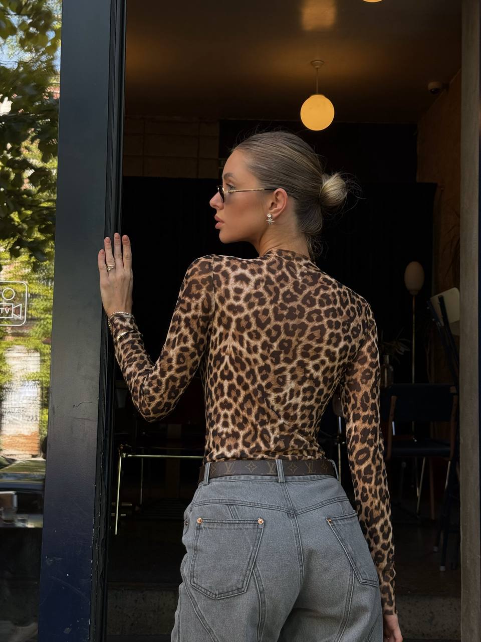 Person wearing a leopard print top and gray pants standing outside a building.