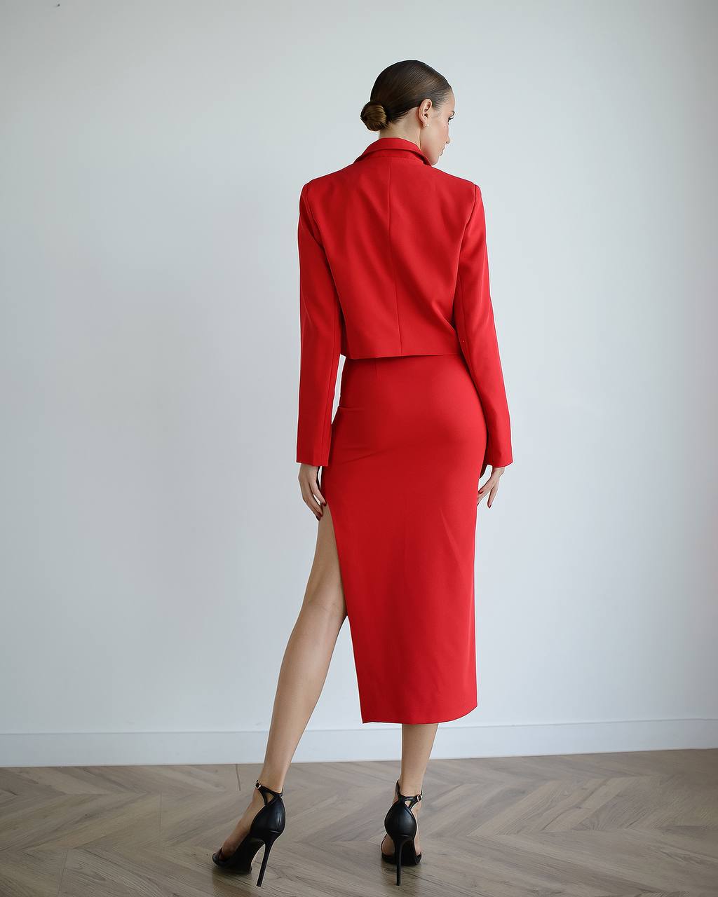 Woman wearing a red suit with a high slit on a plain background