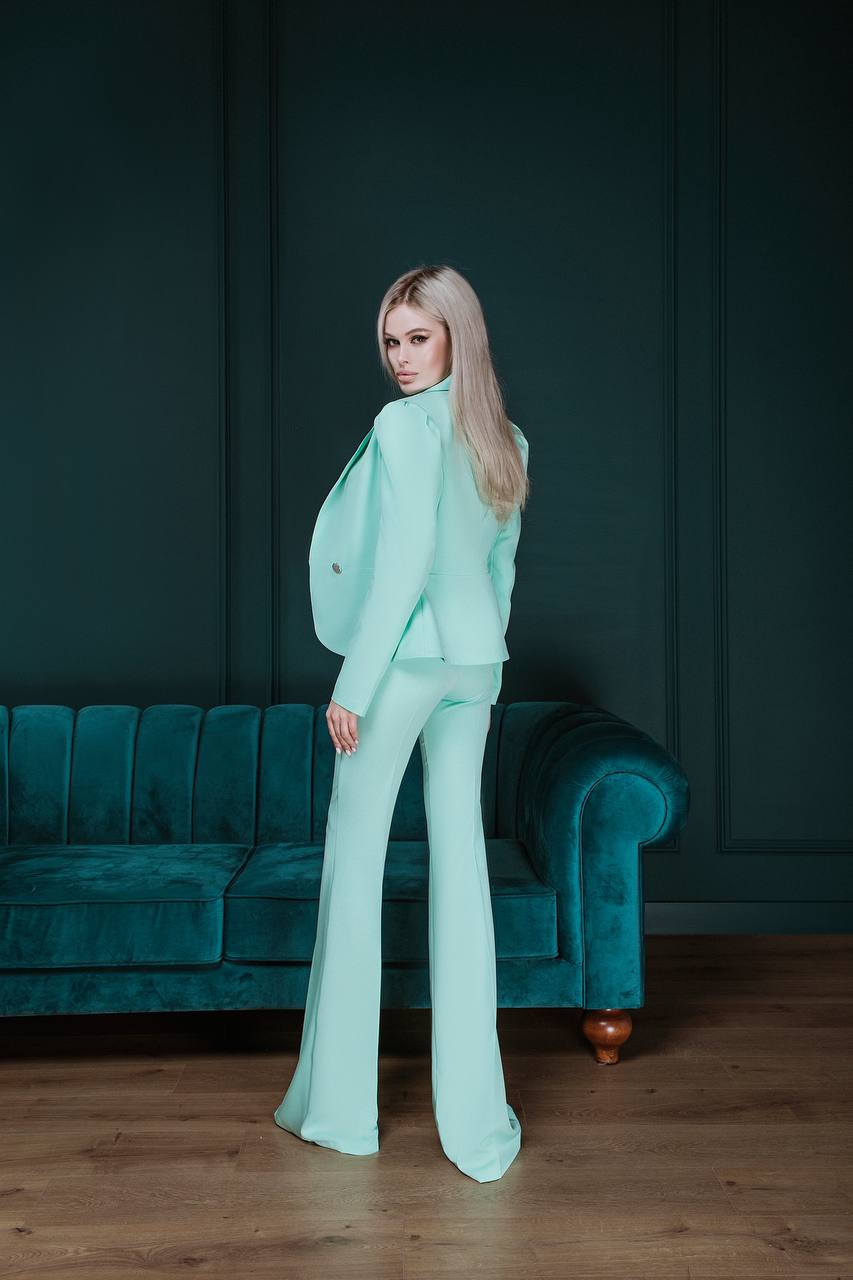 Woman in a light green suit standing in a room with a teal sofa.