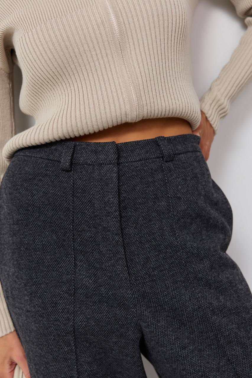 Person wearing a beige sweater and dark gray textured pants on a white background