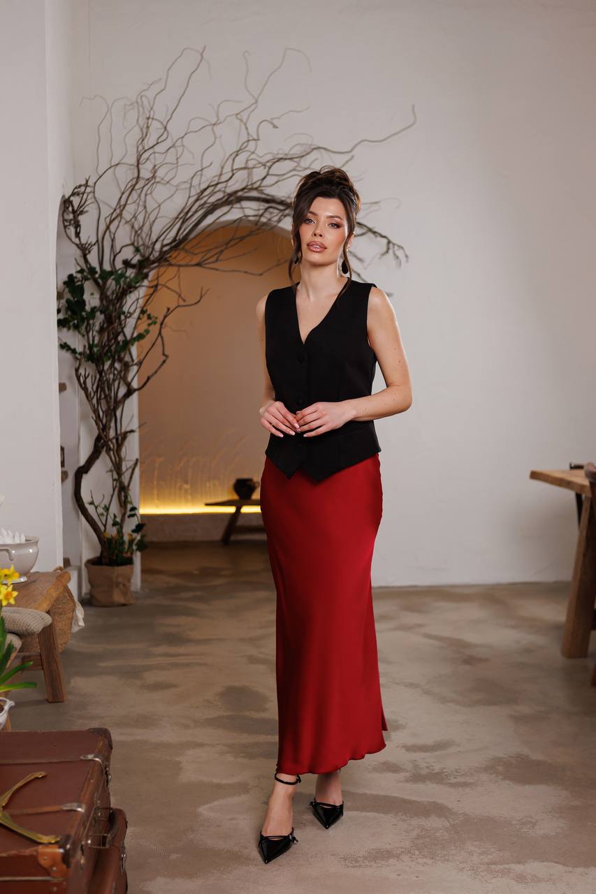 Woman in a black top and red skirt standing in an indoor setting with minimal decor.