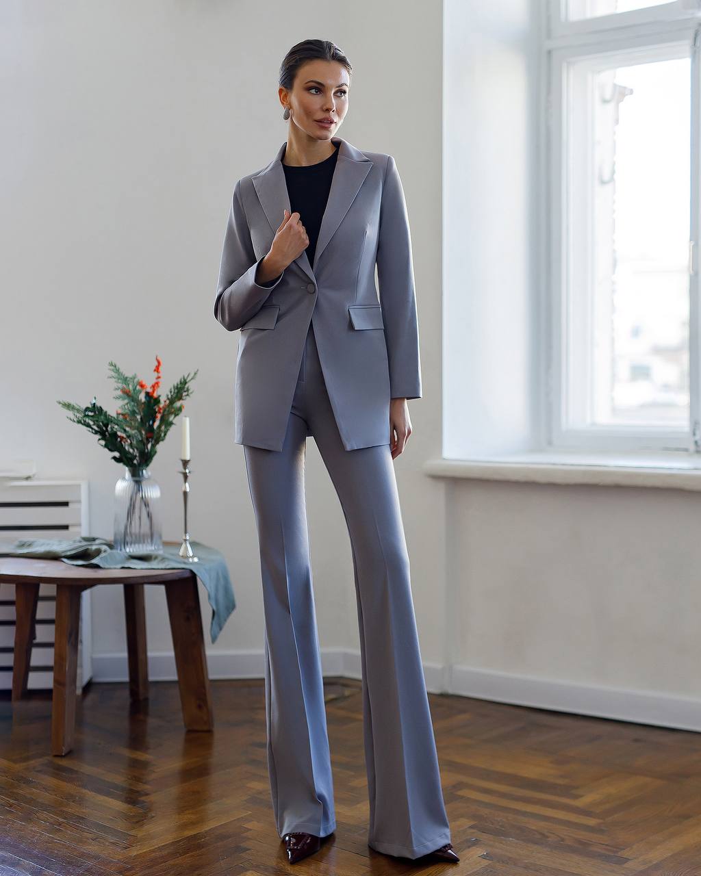 Woman in a light gray suit standing in a room with a table and window.