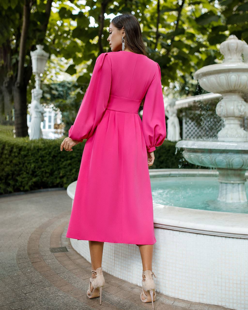 Woman in a pink dress standing near a fountain with greenery in the background
