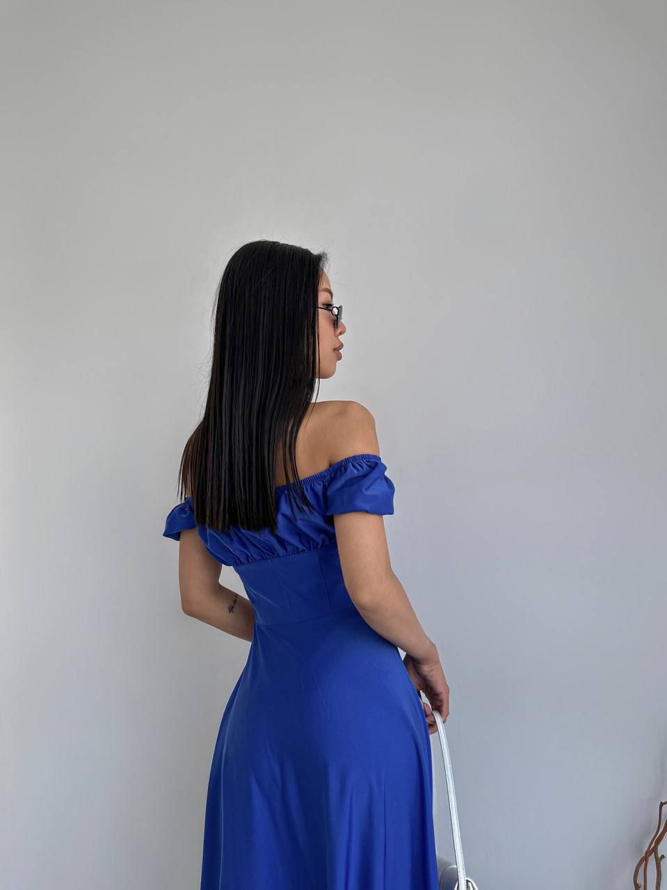 Woman in a blue off-shoulder dress standing against a plain background