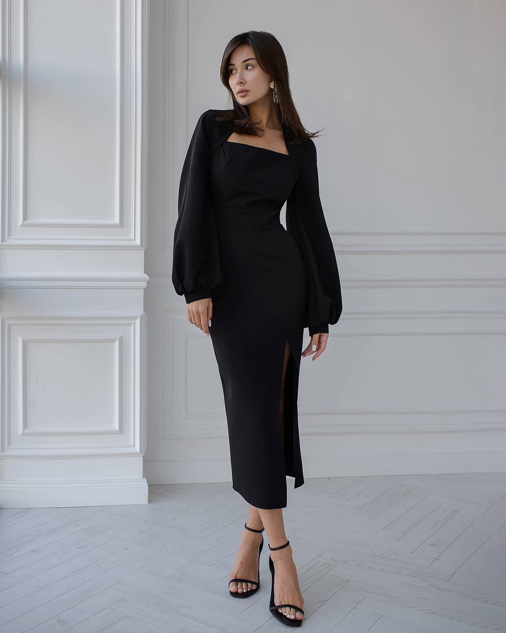 Woman wearing a black dress with long sleeves in a minimalistic setting