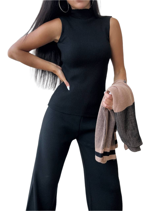 Woman wearing a black sleeveless top and pants holding a jacket on a white background
