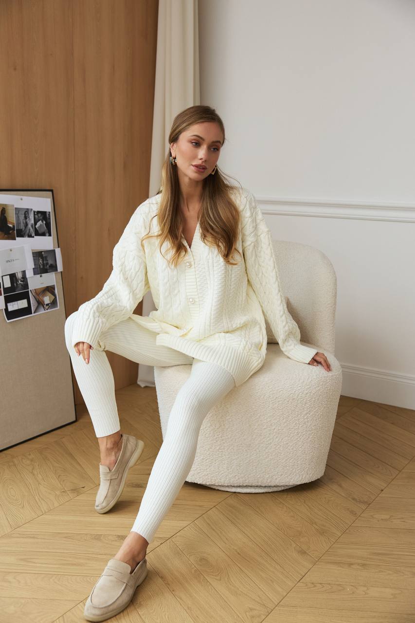 Woman in a white outfit sitting on a white chair in a room with wooden floor and white walls.