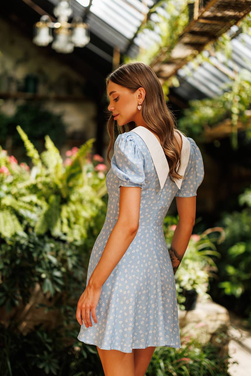 Woman in a light blue dress with white polka dots standing in a garden.