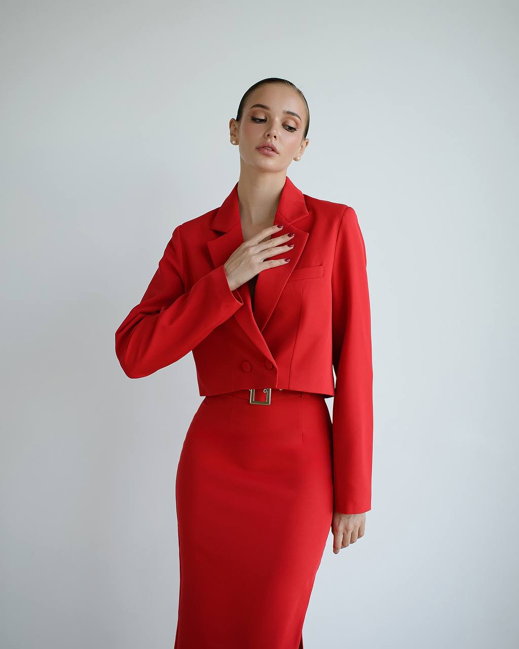Woman wearing a red outfit with a matching jacket and skirt on a plain background