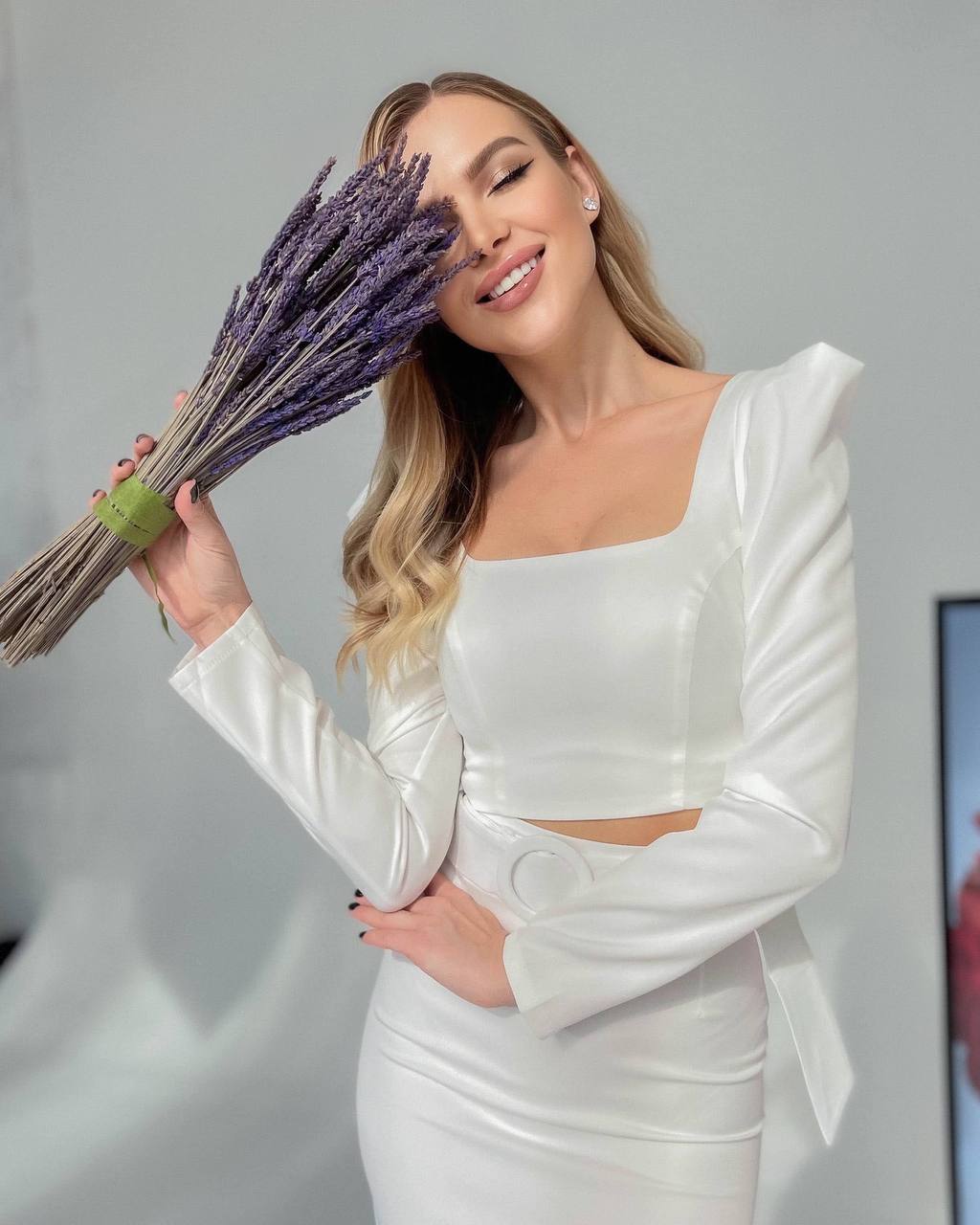 Woman in a white outfit holding a bundle of lavender against a gray background
