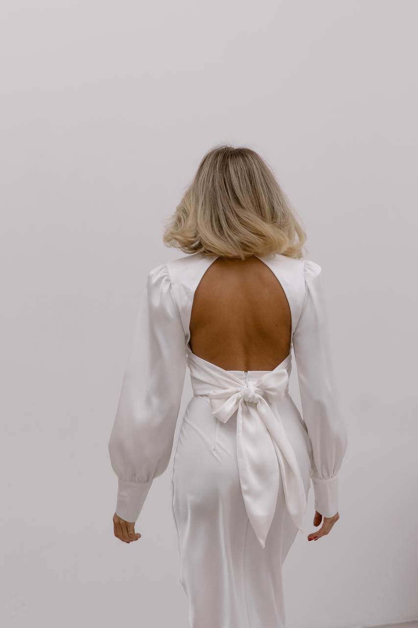 Woman wearing a white dress with a backless design and bow detail on a plain background