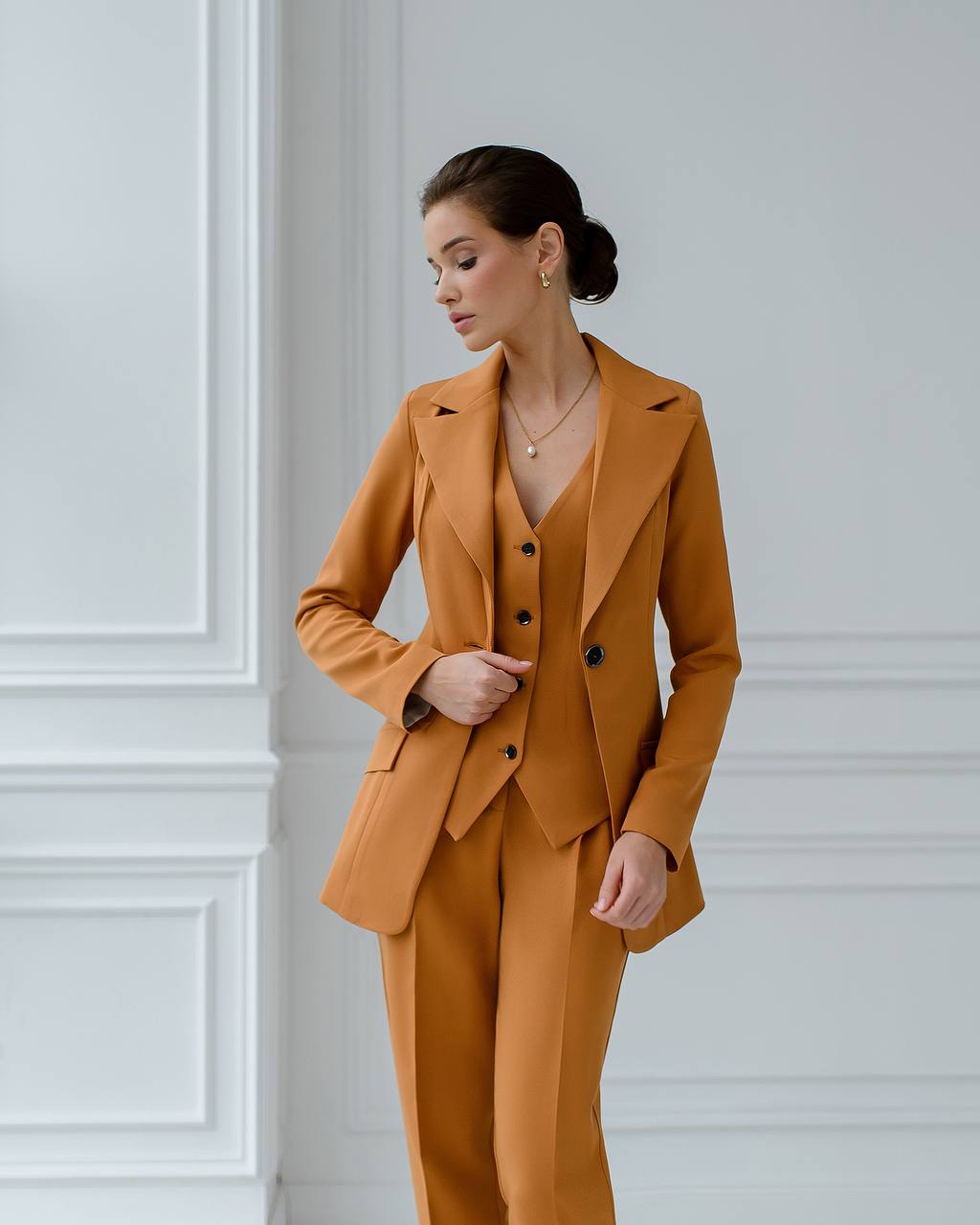 Woman wearing a mustard yellow suit against a white paneled wall