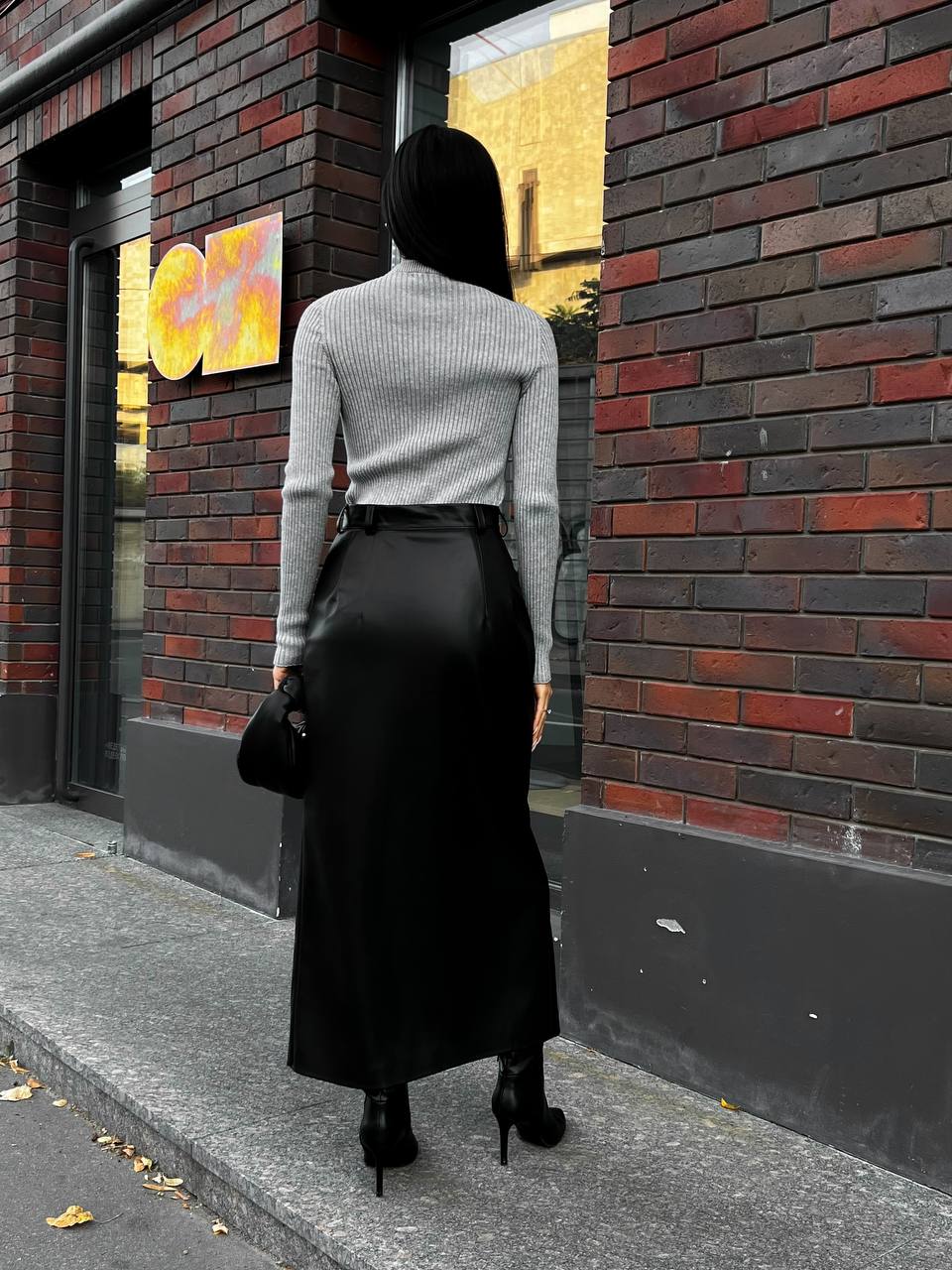 Person wearing a gray sweater and black skirt standing against a brick wall.