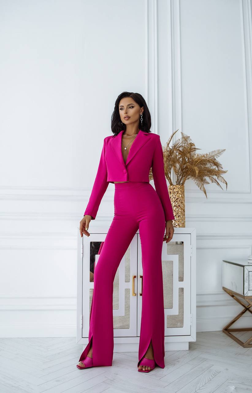 Woman in a bright pink suit standing in a stylish interior setting.