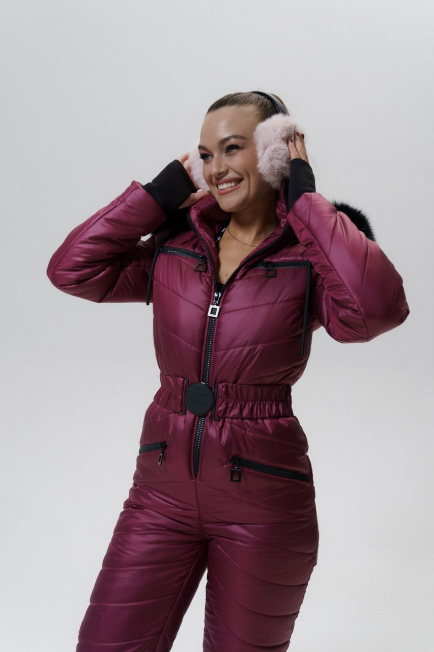 Woman wearing a maroon snowsuit with pink earmuffs on a white background