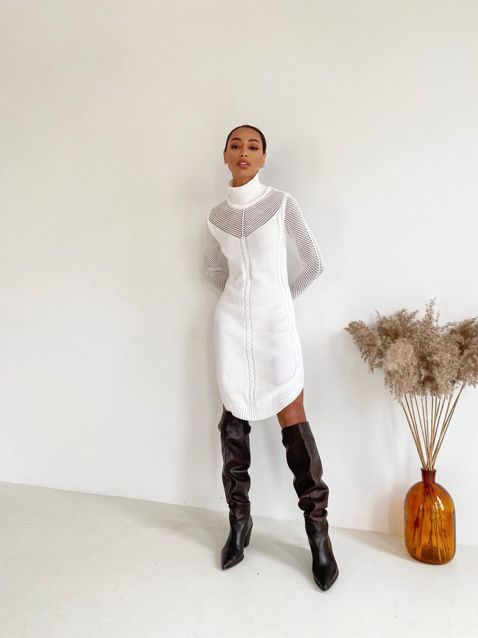 Person wearing a white dress with gray mesh panels and black knee-high boots, standing against a plain background.
