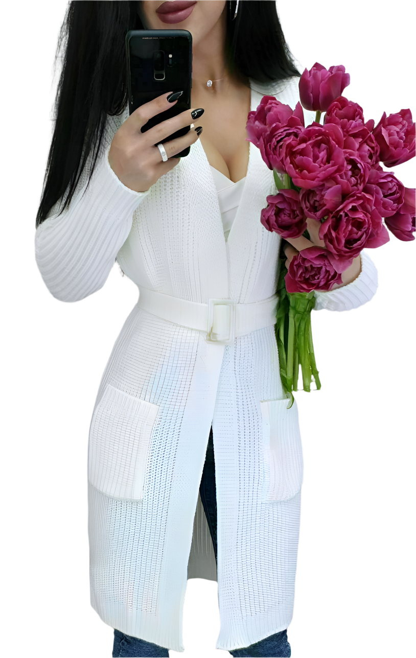 Person wearing a white cardigan holding pink flowers and a phone.