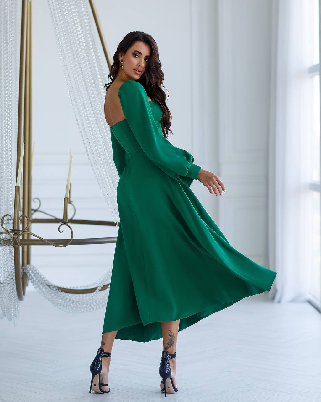 Woman in a green dress standing in a bright room with white curtains.
