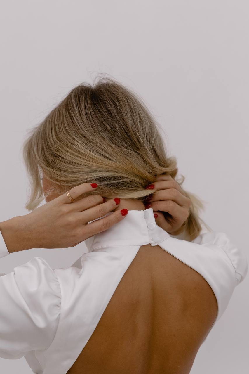 Person with blonde hair tying a white shirt on a plain background