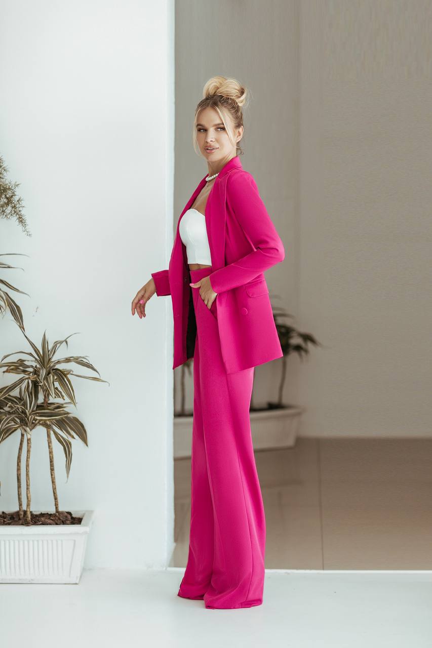 Woman in a bright pink suit standing indoors with a neutral background