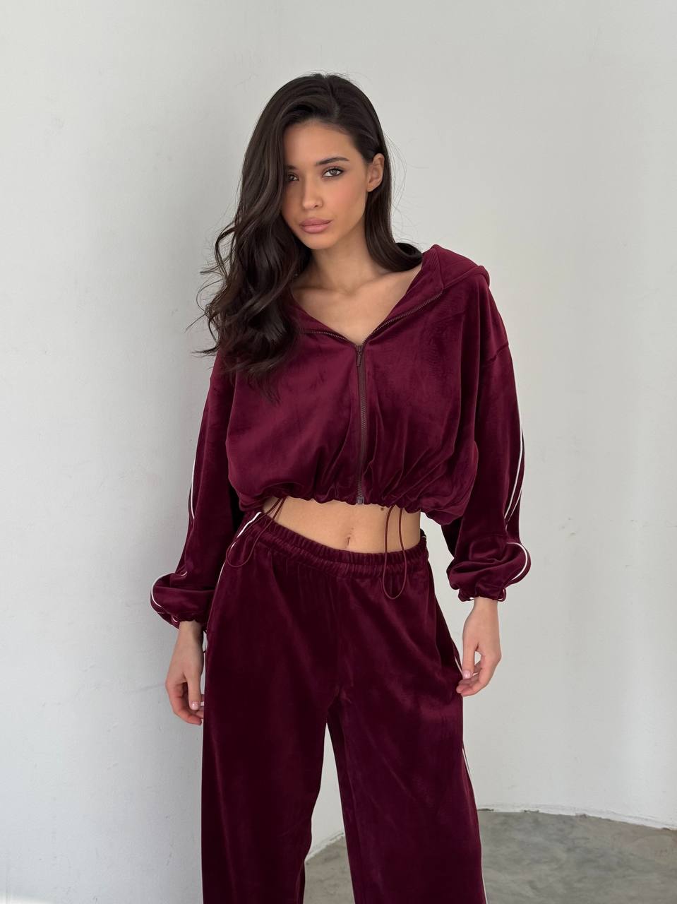 Woman wearing a burgundy velour tracksuit against a plain background