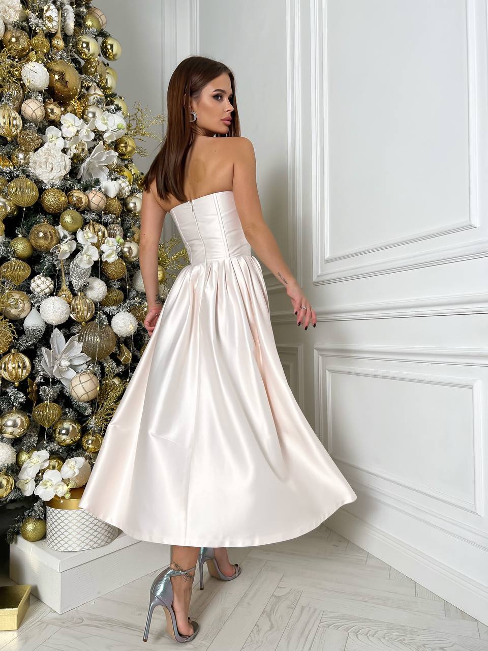 Woman in a white strapless dress standing next to a decorated Christmas tree.