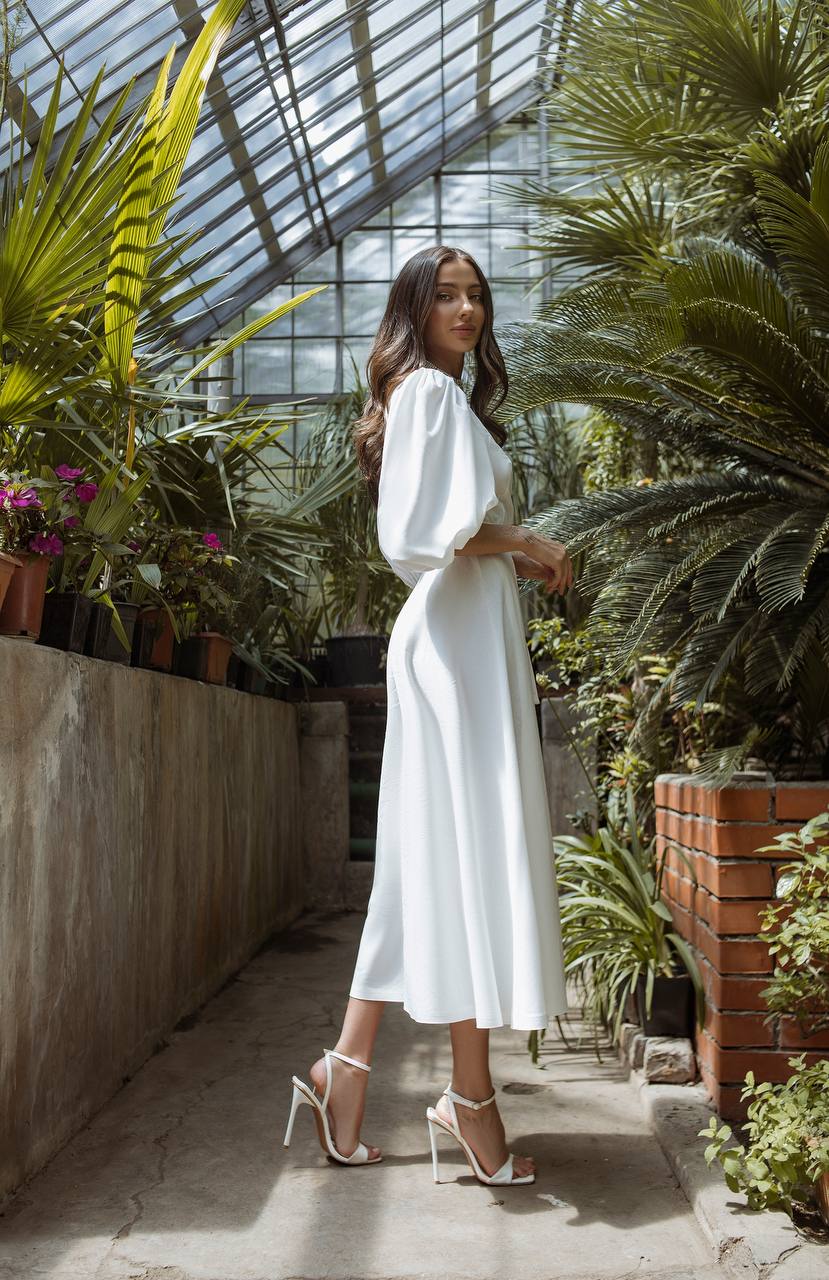 Woman in a white dress standing in a greenhouse filled with plants