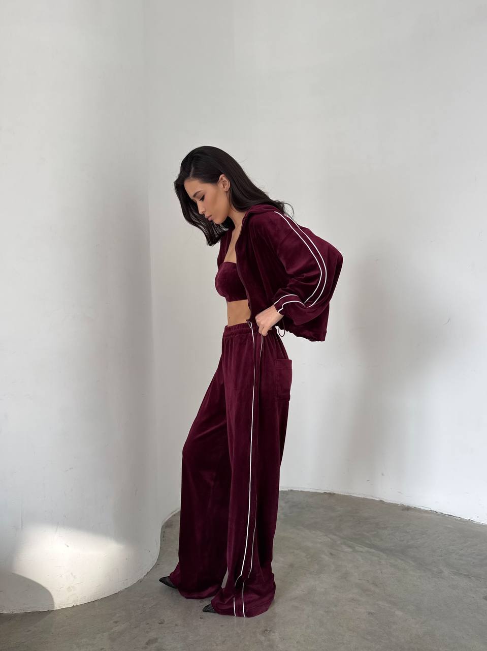 Woman wearing a burgundy velvet tracksuit against a plain white wall.