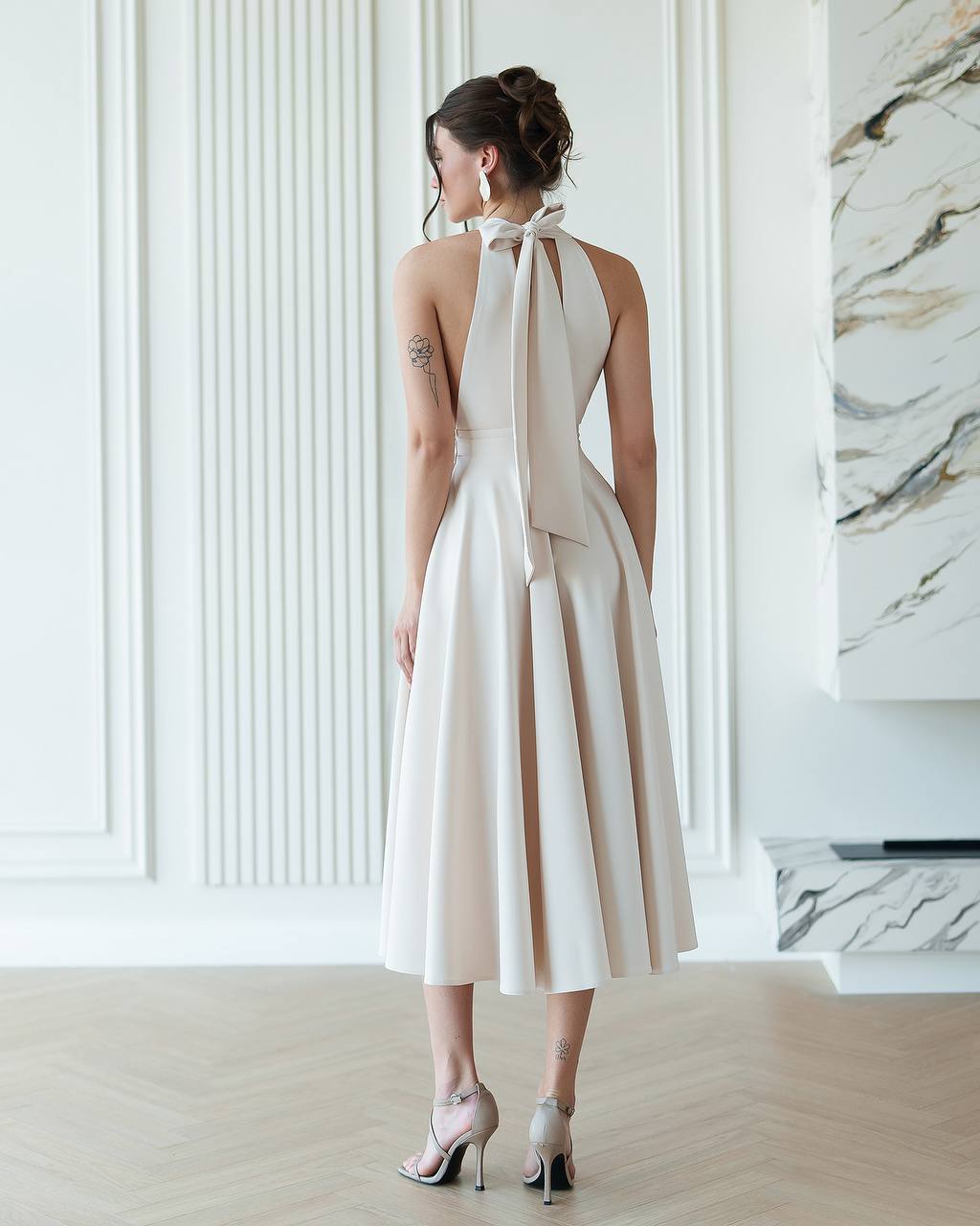 Woman wearing a white halter neck dress with a bow detail in a modern interior setting.