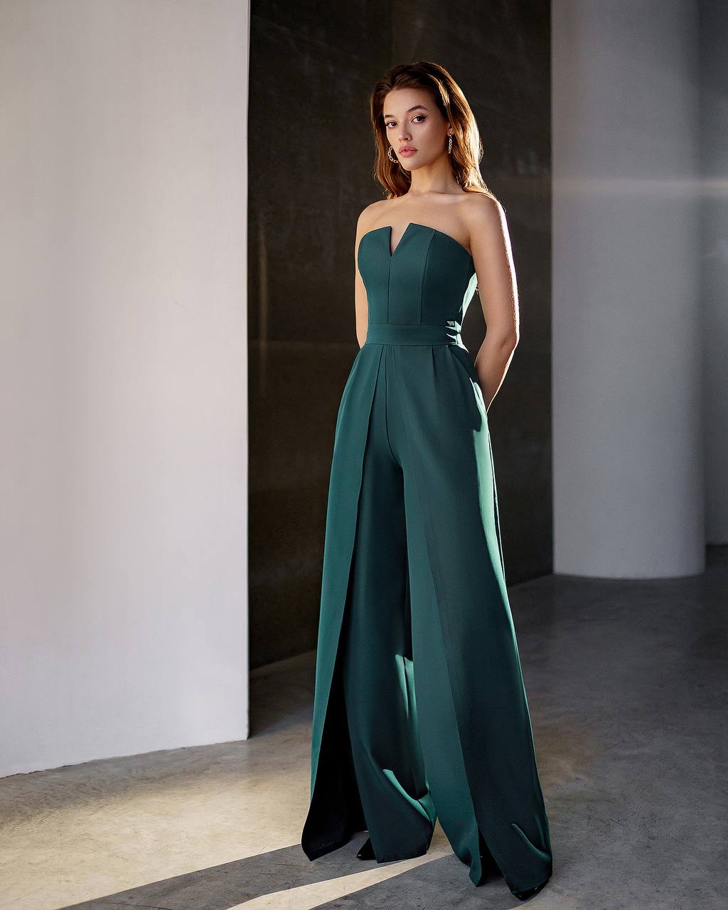 Woman wearing a strapless green gown standing against a neutral wall.
