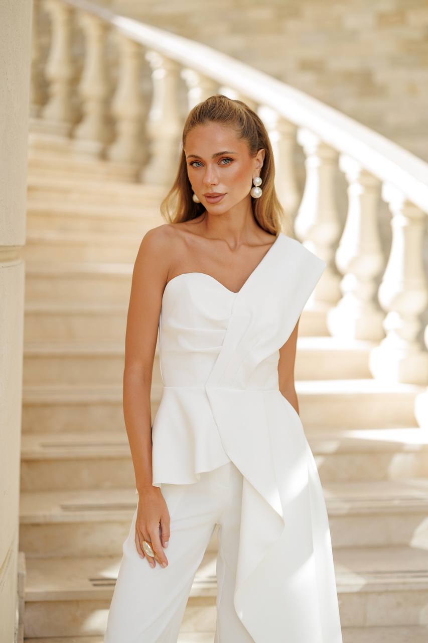 Woman in a white strapless outfit standing on a staircase with marble railings.