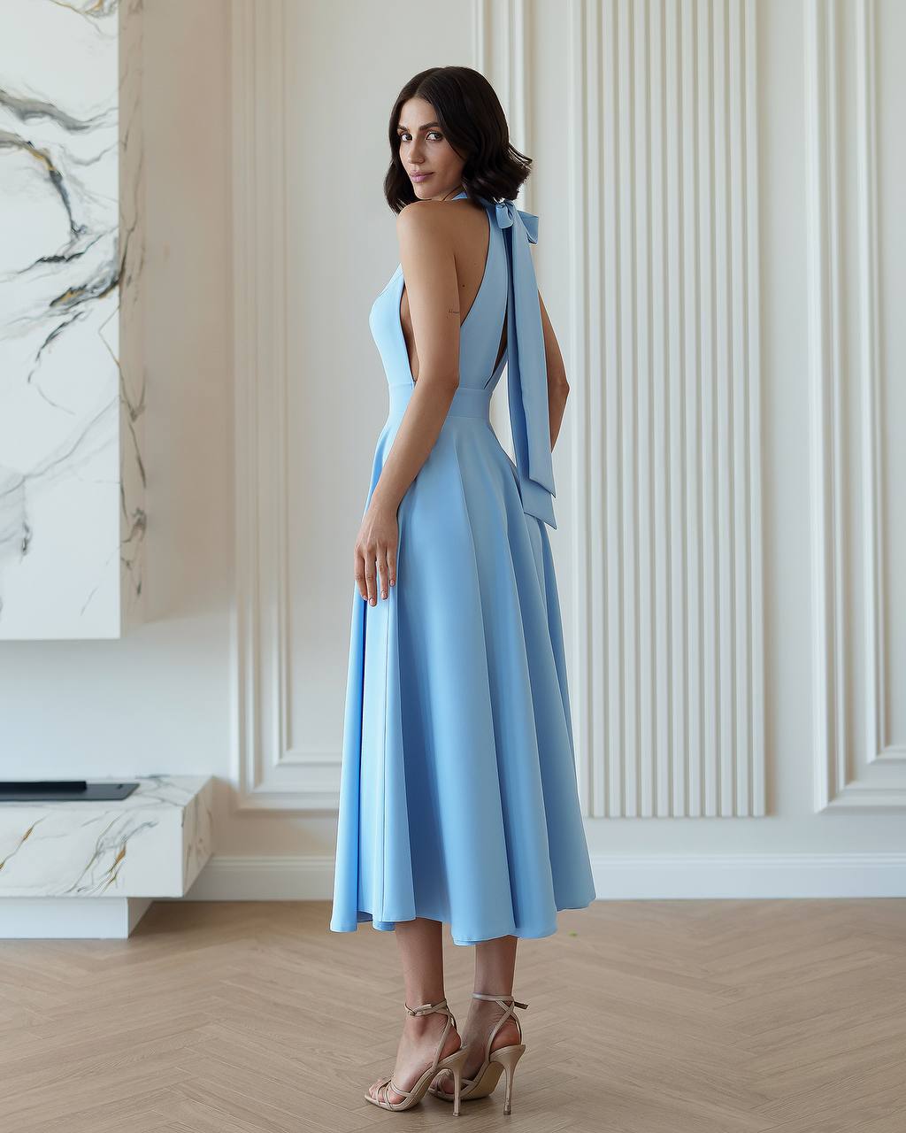 Woman wearing a light blue dress with a bow detail in an elegant room.