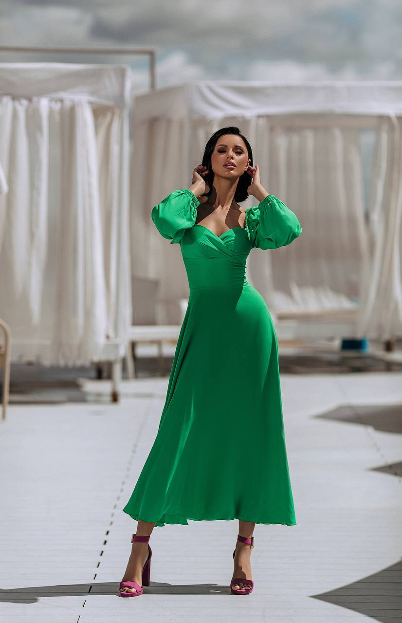 Woman in a green dress standing on a rooftop with white curtains in the background