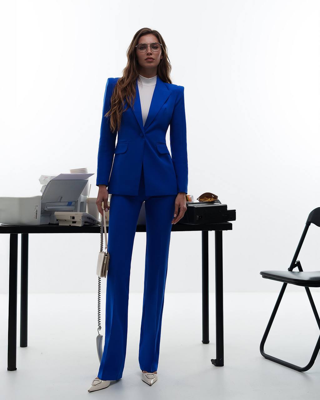 Woman in a blue suit standing in an office setting with a white background