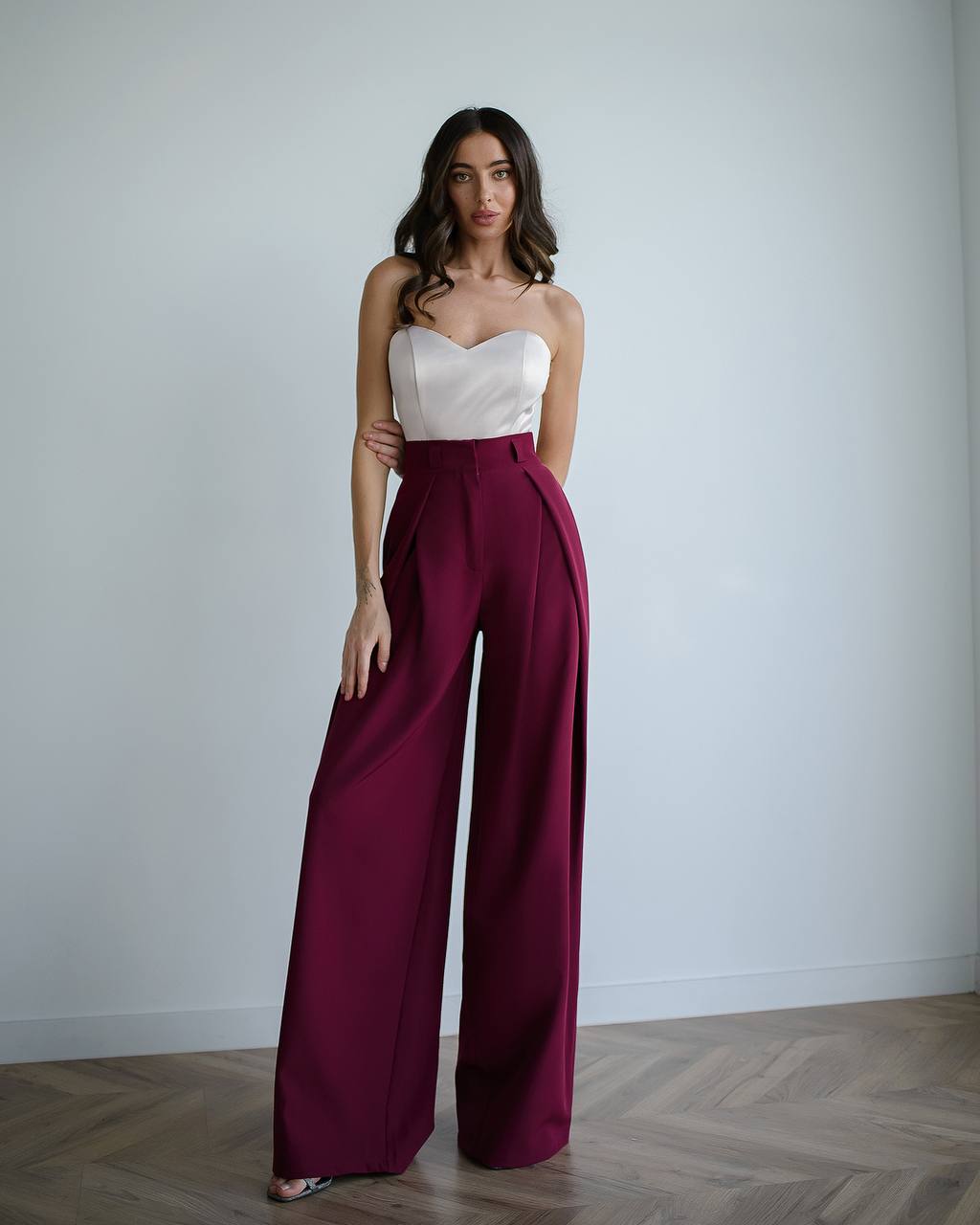 Woman wearing a white strapless top and maroon high-waisted pants against a plain background