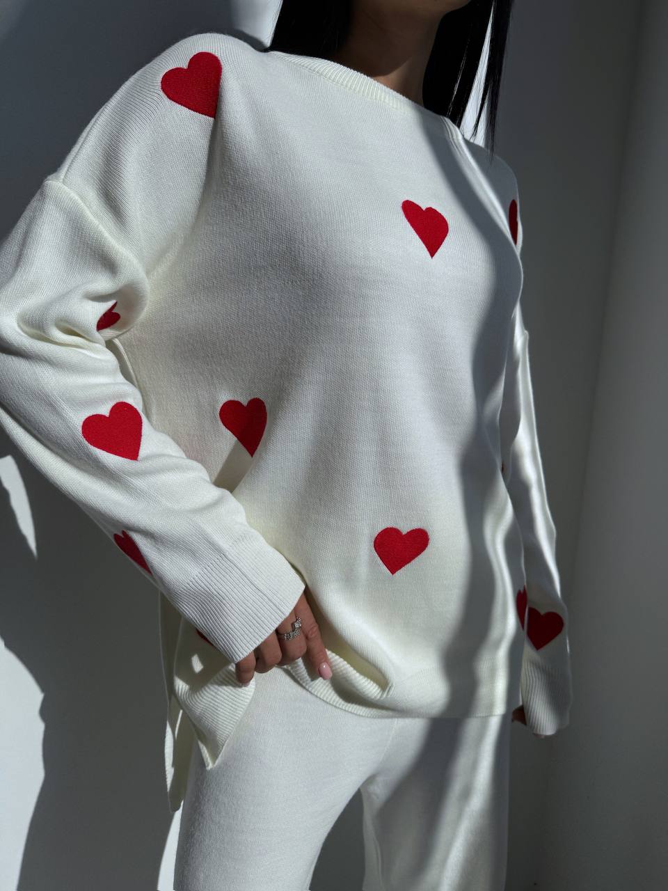 White sweater with red heart patterns worn by a person against a neutral background